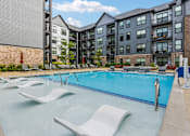 Thumbnail 1 of 23 - A swimming pool with lounge chairs and a building in the background.