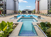 Thumbnail 2 of 23 - A large outdoor swimming pool surrounded by lounge chairs and plants.