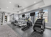 Thumbnail 19 of 23 - A gym with treadmills, elliptical machines, and a fan.