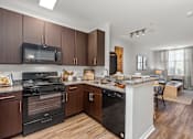Thumbnail 17 of 31 - A kitchen with dark wood cabinets and a black oven. at Merion Riverwalk Apartment Homes, Shelton, CT, 06484