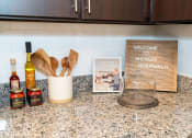Thumbnail 5 of 26 - a kitchen counter with wooden spoons and a bottle of wine and a book at Merion Riverwalk Apartment Homes, Shelton, 06484