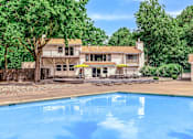 Thumbnail 14 of 27 - A swimming pool in front of a house surrounded by trees.