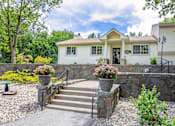 Thumbnail 10 of 27 - A house with a stone wall and steps leading to the front door.