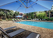 Thumbnail 4 of 34 - A pool surrounded by a patio with chairs and umbrellas.