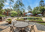 Thumbnail 6 of 34 - A patio with a table and chairs is surrounded by greenery.