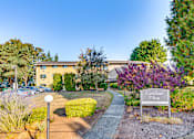 Thumbnail 2 of 17 - The image shows a sign that reads "Kirkland Place" in front of a building with a parking lot and trees in the background.