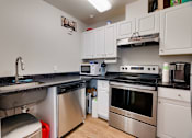 Thumbnail 17 of 27 - A kitchen with white cabinets and black countertops.