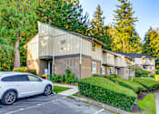 Thumbnail 2 of 9 - A white car is parked in front of a building with a tree in front of it.