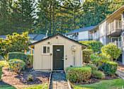 Thumbnail 8 of 9 - A small house with a green door is surrounded by bushes and trees.