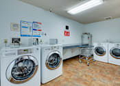 Thumbnail 15 of 18 - A laundry room with a row of washers and dryers.