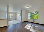 Thumbnail 21 of 33 - A large empty room with wooden floors and a window showing green trees outside.