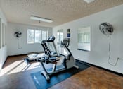 Thumbnail 10 of 18 - A gym with a treadmill and a fan.