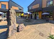 Thumbnail 32 of 33 - A large rock sits in the middle of a plaza in front of a building with a sign that reads "Experience".