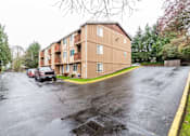 Thumbnail 24 of 29 - A large apartment building is situated on a street with a parking lot in front.