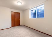 Thumbnail 11 of 29 - A room with a carpeted floor, a brown door, and a window showing a view of a building outside.