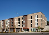 Thumbnail 9 of 22 - A modern apartment building with a mix of beige and brown facades.