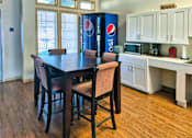 Thumbnail 4 of 19 - A dining table with chairs and a Pepsi fridge in the background.