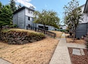 Thumbnail 15 of 21 - A grey house with a stone wall and a sidewalk.