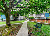 Thumbnail 11 of 19 - A green bench is on the grass next to a sidewalk.
