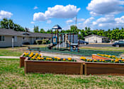 Thumbnail 8 of 19 - A playground with a swing set and a wooden fence with yellow flowers in the foreground.