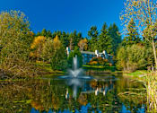 Thumbnail 3 of 18 - A serene landscape with a fountain in the middle of a pond surrounded by trees.