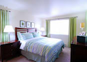 Thumbnail 7 of 18 - A bedroom with a bed, nightstands, and a window with green curtains.