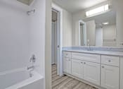 Thumbnail 26 of 31 - A white bathroom with a tub, sink, and mirror.