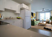 Thumbnail 1 of 6 - A kitchen with white cabinets and a green couch in the living room.