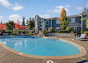 Thumbnail 14 of 16 - A swimming pool in front of a building with trees in the background.