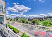 Thumbnail 4 of 40 - A red car is driving on a road with a building on the left.