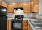 Thumbnail 4 of 16 - A black refrigerator sits next to a black stove in a kitchen with wooden cabinets.