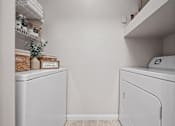 Thumbnail 3 of 57 - In-unit full-size washer and dryer set with overhead shelving and storage space inside a laundry closet at Crescent Apartments in Lenexa, KS.