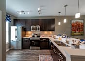 Thumbnail 1 of 15 - A modern kitchen with dark wood cabinets and stainless steel appliances.