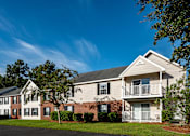 Thumbnail 9 of 14 - A large apartment complex with a green lawn in front.