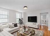 Thumbnail 24 of 24 - A living room with a white couch, a coffee table, and a flat screen TV.