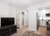 Thumbnail 15 of 37 - a living room with a tv and a kitchen with a refrigerator