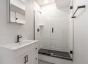 Thumbnail 12 of 35 - A white bathroom with a sink, mirror, and walk-in shower.