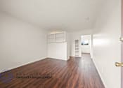 Thumbnail 7 of 17 - A room with wooden floors and white walls, with a door on the right side.