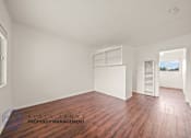 Thumbnail 5 of 17 - A room with wooden floors and white walls, with a window on the left and a door on the right.