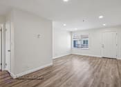 Thumbnail 16 of 21 - A spacious room with wooden flooring and white walls, with a window showing a view of a balcony.