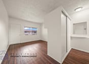 Thumbnail 3 of 17 - A room with wooden floors and white walls, with a window showing a view of a building outside.