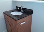 Thumbnail 8 of 10 - A brown cabinet with a black counter top and a white sink.