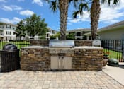 Thumbnail 33 of 40 - A stone fireplace with a grill on top is in the middle of a brick patio.