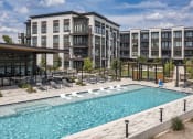 Thumbnail 16 of 22 - a swimming pool with chaise lounge chairs and a building in the background