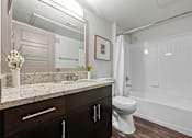 Thumbnail 16 of 36 - A white toilet sits in a bathroom with a marble countertop and a white bathtub.