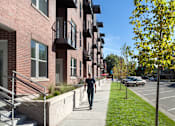 Thumbnail 8 of 16 - a man walking down a sidewalk in front of a row of apartment buildings