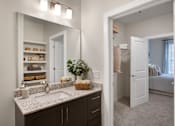 Thumbnail 15 of 47 - A bathroom with a large mirror above a sink with a basket of towels on the counter.