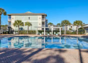 Thumbnail 20 of 30 - A swimming pool in front of a building with a clear blue sky.