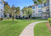 Thumbnail 28 of 29 - a sidewalk leading to an apartment building with green grass and trees