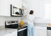 Thumbnail 12 of 26 - a woman cleaning a microwave in a kitchen